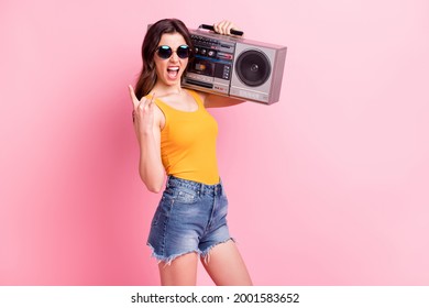 Photo of rude funky lady dressed yellow tank-top dark glasses holding boom box showing hard rock sign isolated pink color background
