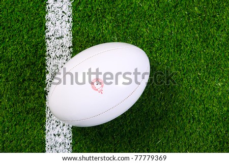 Photo of a rugby ball on a grass next to the white line, shot from above.