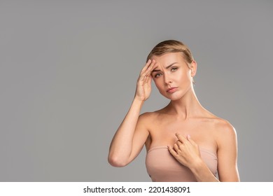 Photo Of Sad Woman With Headache. Blonde Girl With Short Hair Holding Hand On The Forehead, Looking At The Camera. A Lot Of Copy Space On Studio Background.