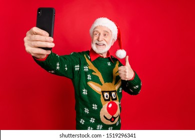 Photo Of Santa Man Holding Telephone Making Selfies For X-mas Blog Raising Thumb Up Express Cool Attitude Wear X-mas Ugly Ornament Sweater Cap Isolated Red Background