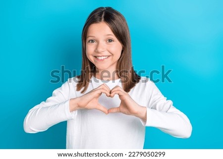 Photo of satisfied cute schoolgirl with straight hairdo dressed white shirt showing heart symbol isolated on blue color background