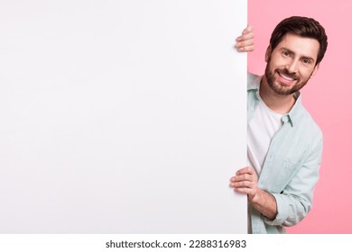 Photo of satisfied man hide behind white huge placard empty space looking camera enjoy new website app isolated on pink color background