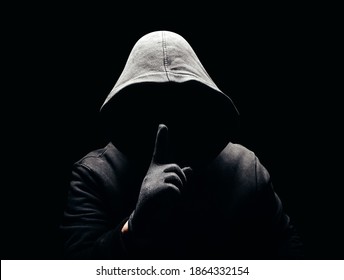 Photo of a scary horror man in hoodie showing silence hand sign in dark. - Shutterstock ID 1864332154