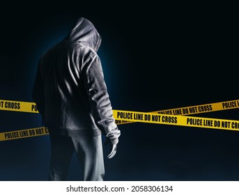 Photo of scary horror stranger stalker or serial killer man in black hood and clothing on dark blue background with police lines.