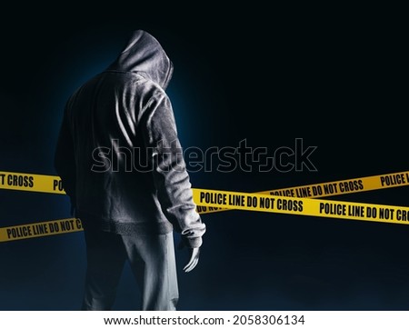 Photo of scary horror stranger stalker or serial killer man in black hood and clothing on dark blue background with police lines.
