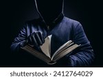 Photo of scary shaded hooded man holding book and turning the pages on dark background. Horror book concept.