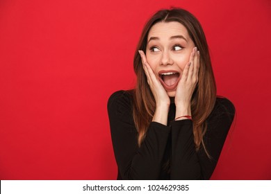 Photo of screaming excited young woman standing isolated over red background. Looking aside.