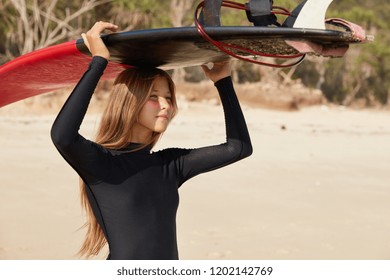 Photo Of Self Assured Professional Woman Wears Beaver Tail, Waits For Big Surfs, Stands At Bone Yard, Being Goofy Foot, Ready To Hit Surf, Poses Against Sandy Beach, Afraids Of Rip, Enjoys Spare Time