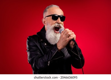 Photo senior excited man sing karaoke microphone rocker wear eyeglasses isolated over red color background