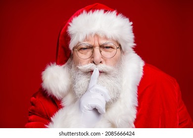 Photo of serious confident retired man wear santa claus costume spectacles fingers lips asking keep silence isolated red color background - Powered by Shutterstock