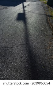 A Photo Of A Shadow Being Casted On A Road Next To A Building By An Adjacent Telephone Pole Standing Tall In The Sunlight.