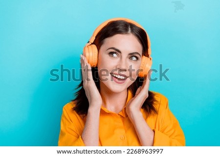 Photo of shiny dreamy woman dressed orange shirt enjoying music headphones looking empty space isolated teal color background