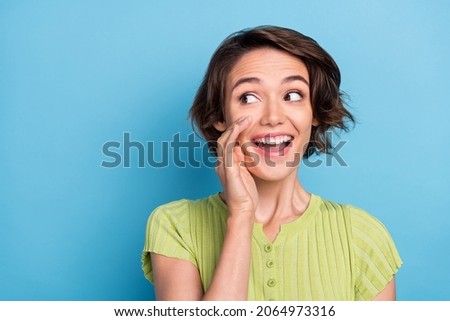 Photo of shiny excited young lady wear green t-shirt arm mouth shouting announcement looking empty space isolated blue color background