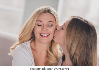Photo of shiny lovely daughter mom wear white t-shirts kissing cheek cheekbone hugging sitting sofa indoors inside room home
