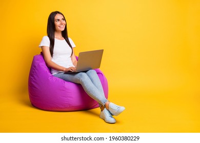 Photo of shiny young lady wear white t-shirt sitting beanbag typing modern gadget looking empty space isolated yellow color background