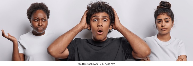 Photo of shocked curly haired Hindu man stares with disbelief displeased African woman keeps palm raised up being dissatisfied Iranian girl keeps arms folded isolated over white studio background - Powered by Shutterstock