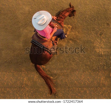 photo shoot seen from above of a cowboy woman riding her horse doing a spin with a hot light in the late afternoon
