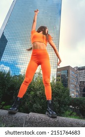 Photo shoot of stylish caucasian hip hop dancer posing having fun in orange leggings and top gymnastic jumpsuit, enjoy the urban town as background. City buildings shooting of moving fitness model