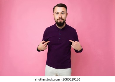 Photo shot of handsome self-confident and good looking young brunet bearded man wearing casual and stylish purple longsleeve poising isolated on pink background with empty space for text and showing