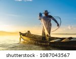 Photo shot of water spatter from fisherman while throwing fishing net from boat. Silhouette of asian fishermen with fishing net in morning sunshine along harbor. Stop motion water drop on sea.