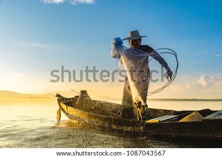 Photo shot of water spatter from fisherman while throwing fishing net from boat. Silhouette of asian fishermen with fishing net in morning sunshine along harbor. Stop motion water drop on sea.