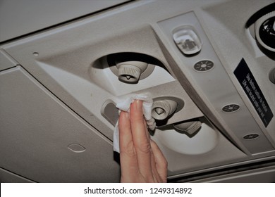 Photo Showing Woman's Hand Cleaning The Air Vents In An Airplane With A White Disinfectant Wipe