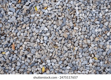 The photo shows a close-up of a gravel surface covered with small, multicolored pebbles. A few yellow and brown leaves are scattered among the pebbles. - Powered by Shutterstock