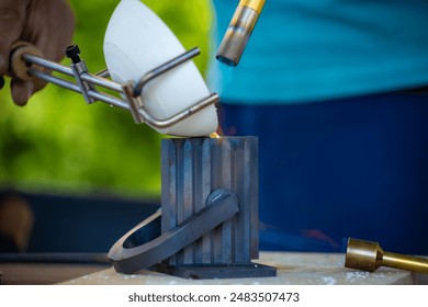 The photo shows a close-up of a person pouring molten silver into a mold. The silver is glowing white-hot, and it is carefully being poured into the mold to create a specific shape. - Powered by Shutterstock