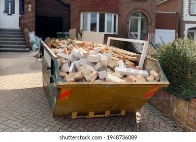 Photo shows front part of full industrial rubbish skip for background use. Space to add text on surrounding blurry area near the bin, driveway, green trees bush, houses. Renovate, skip hire concept.