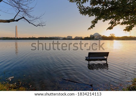 Photo shows high tide at Tidal Basin where the water has flooded the pavement and part of the chair was submerged in water on a clear sky morning. The chair is in focus while the rest is off focus.