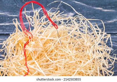 Das Foto zeigt eine Nadel mit rotem Faden mit Holzwolle