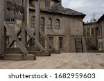 The photo shows part of a dark medieval or pirate town with a guillotine on a wooden platform. In the background, houses with broken windows, desolation and destruction as during the plague pandemic.