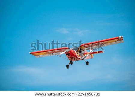 The photo shows a single bright red airplane performing a beautiful maneuver in a clear and sunny blue sky. The airplane appears strong and energetic with its wide-open wings and smooth aerodynamic sh