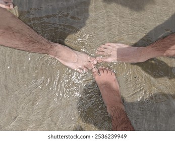 The photo shows three pairs of feet touching in shallow water. The water is rippling and there are shadows from the sun.
 - Powered by Shutterstock