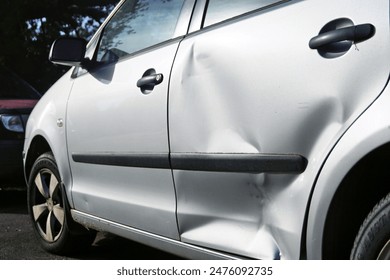 Photo of a silver passenger car with a severe dent on the back door. A car with material damage after a road collision.