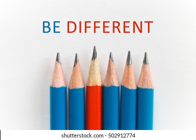 Photo of simple sharp pencils on white desk background, one red among the blue, close up. Flat lay with text "Be different". Stand out from the crowd, leadership concept