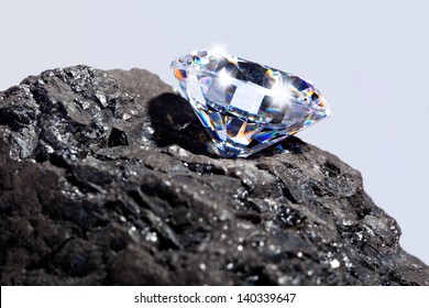 Photo Of A Single Cut Diamond On A Piece Of Coal Against A Plain Background.