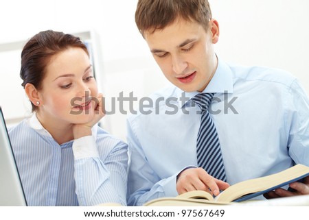 Photo of smart businessman and his pretty colleague reading book in office