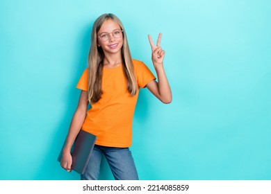 Photo of smart cute little girl wear orange t-shirt toothy smile hold laptop v-sign toothy smile enjoy home education isolated on aquamarine color background