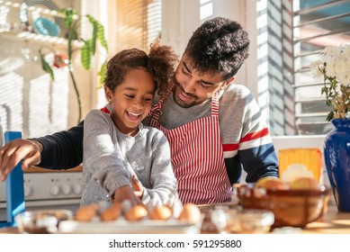 Photo of a smiling african american father and daughter baking in the kitchen and having fun.