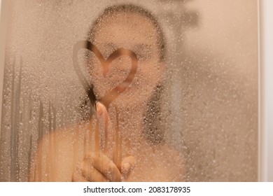 Photo Of Smiling Attractive Young Woman Draws Heart On Weeping Glass Shower Door, Enjoys Rest In Douche, Washing Her Body, Standing Behind Steam Blurred Glass With Water Drops.