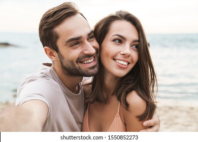 Photo of smiling young couple hugging and taking selfie photo while resting on sunny beach - Shutterstock ID 1550852273