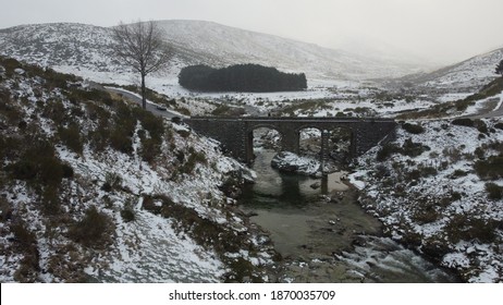 
Photo Of A Snowy Bridge With Snowy Ice With A Person And A River Below The Bridge With A Forest In The Background