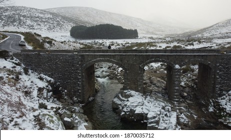 
Photo Of A Snowy Bridge With Snowy Ice With A Person And A River Below The Bridge With A Forest In The Background