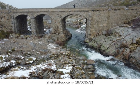 
Photo Of A Snowy Bridge With Snowy Ice With A Person And A River Below The Bridge With A Forest In The Background