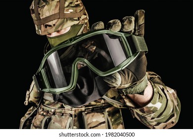 Photo of soldier in level 3 armored vest ammunition, tactical gloves holding tactical goggles on black background.
