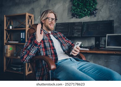 Photo of specialist blond hair young guy sitting on armchair with smartphone having phone call video greetings indoors coworking office - Powered by Shutterstock