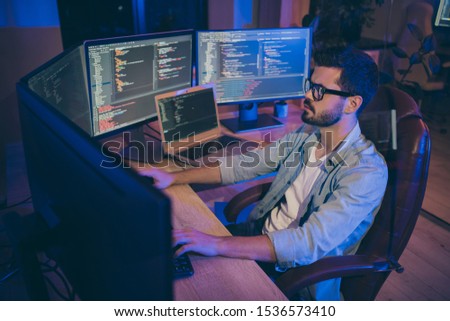 Photo of it specialist guy sitting comfy office chair holding hands on keyboard looking many monitors testing website debugging developer expert dark office indoors