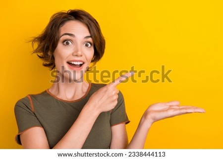 Photo of speechless ecstatic girl dressed khaki t-shirt directing empty space arm hold product isolated on yellow color background