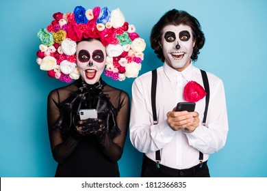 Photo Of Spooky Demon Couple Man Lady Hold Telephones Excited Find Way Become Ghosts Prank Friend Wear Black Dress Death Costume Roses Headband Suspenders Isolated Blue Color Background